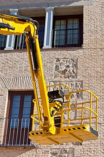 Žlutá výšková plošina před cihlovou fasádou historického domu při čištění fasády v Praze